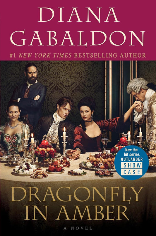 Book cover of 'Dragonfly in Amber' by Diana Gabaldon featuring characters around a table with food. Best print quality in Bangladesh.
